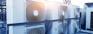 Klimaanlagen-Außengeräte stehen in einer Reihe auf einem Dach in Sonnenlicht, umgeben von Strukturstreben.