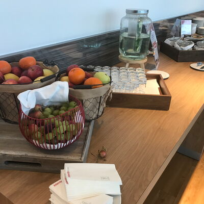 Buffet mit Körben voller Obst, Gläsern, einem Glasbehälter mit Wasser und einem Tablett mit Servietten auf einem Holztisch in einem Seminarraum in Berlin