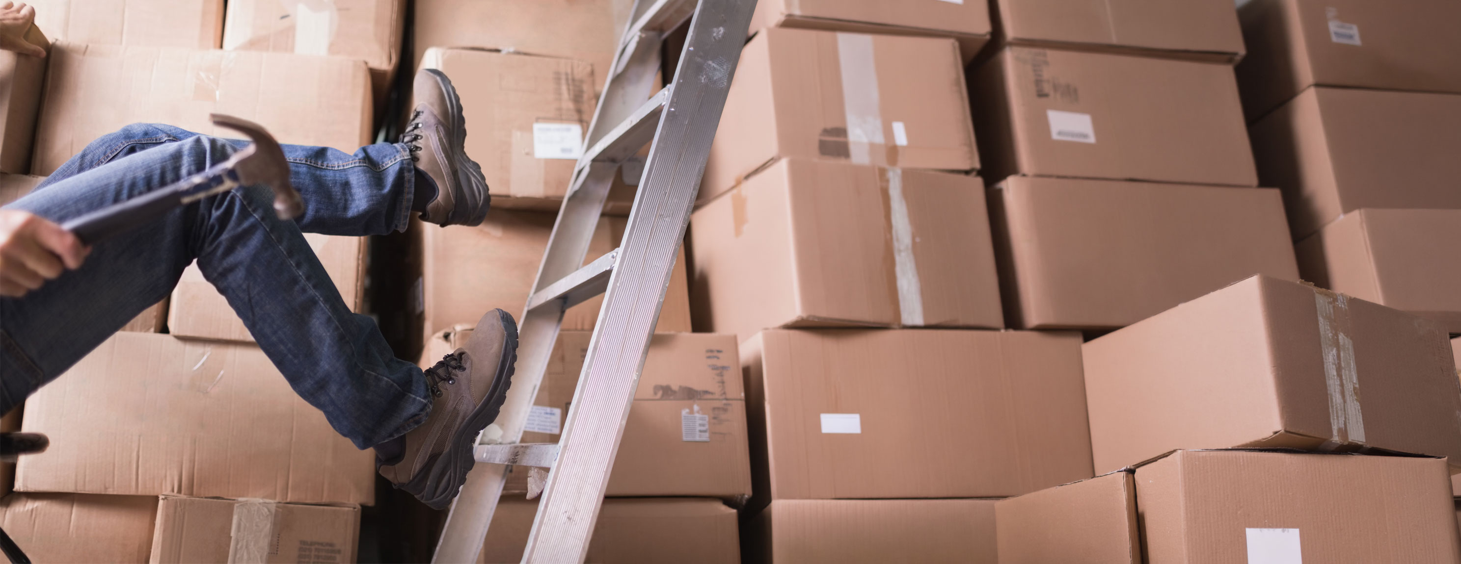 Person fällt von einer Metallleiter vor einem Stapel aus Kartons
